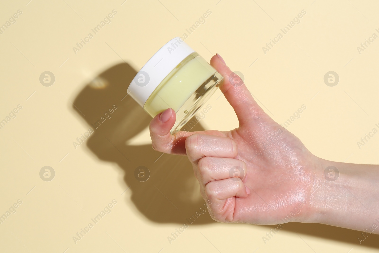 Photo of Woman holding jar of cream on yellow background, closeup