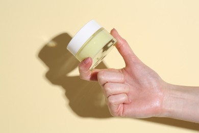 Photo of Woman holding jar of cream on yellow background, closeup