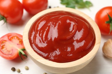 Photo of Delicious ketchup in bowl and tomatoes on white table, closeup