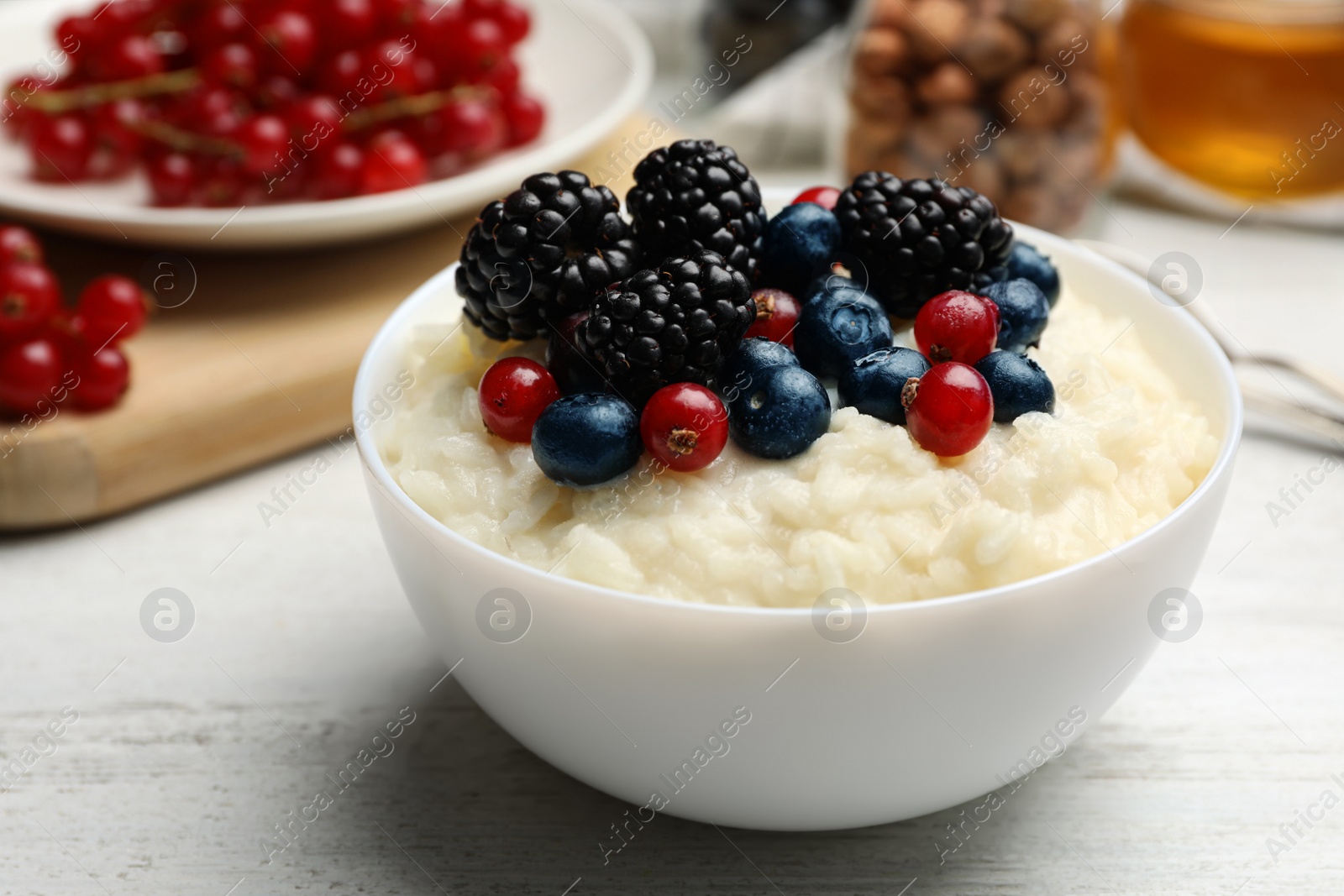 Photo of Delicious rice pudding with berries on white wooden table, closeup