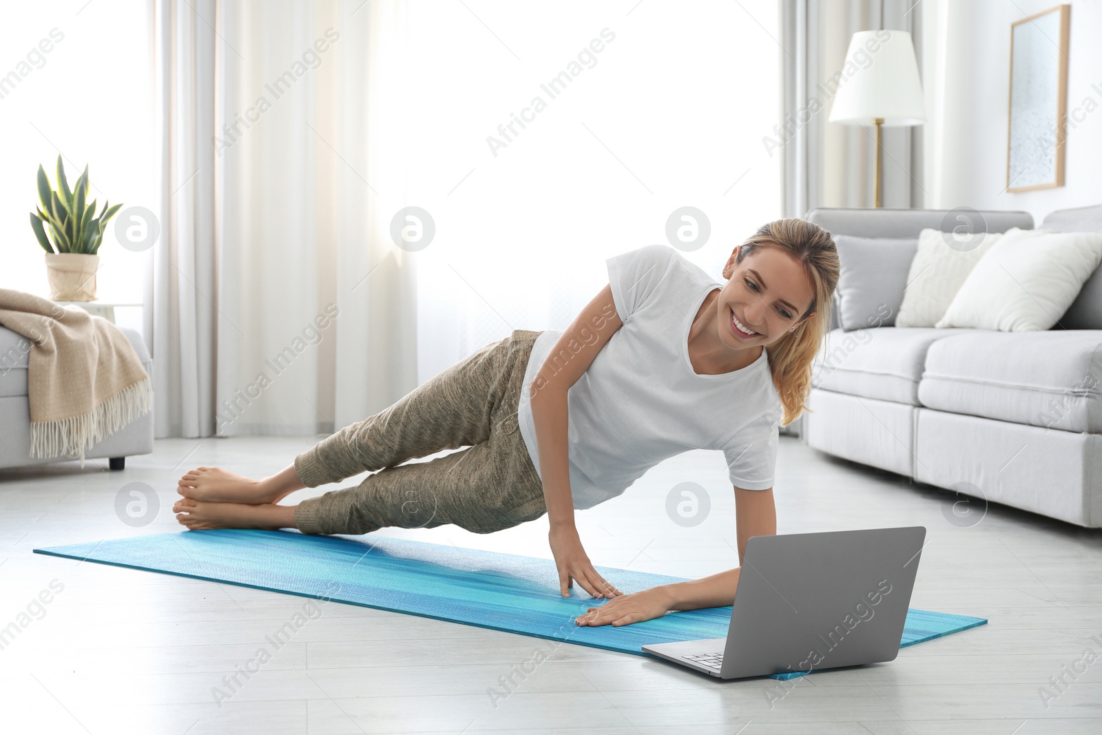 Photo of Woman having online video class via laptop at home. Distance yoga course during coronavirus pandemic