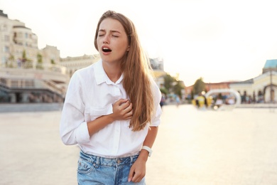 Young woman having heart attack on city street. Space for text