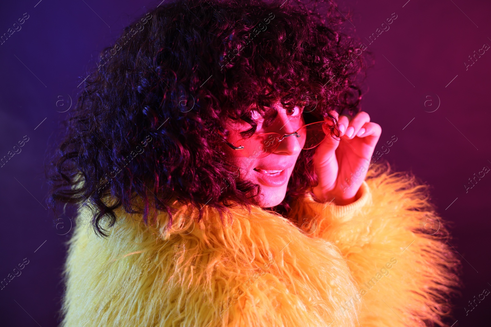 Photo of Beautiful young woman in yellow fur coat and sunglasses on color background in neon lights