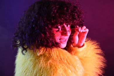 Beautiful young woman in yellow fur coat and sunglasses on color background in neon lights