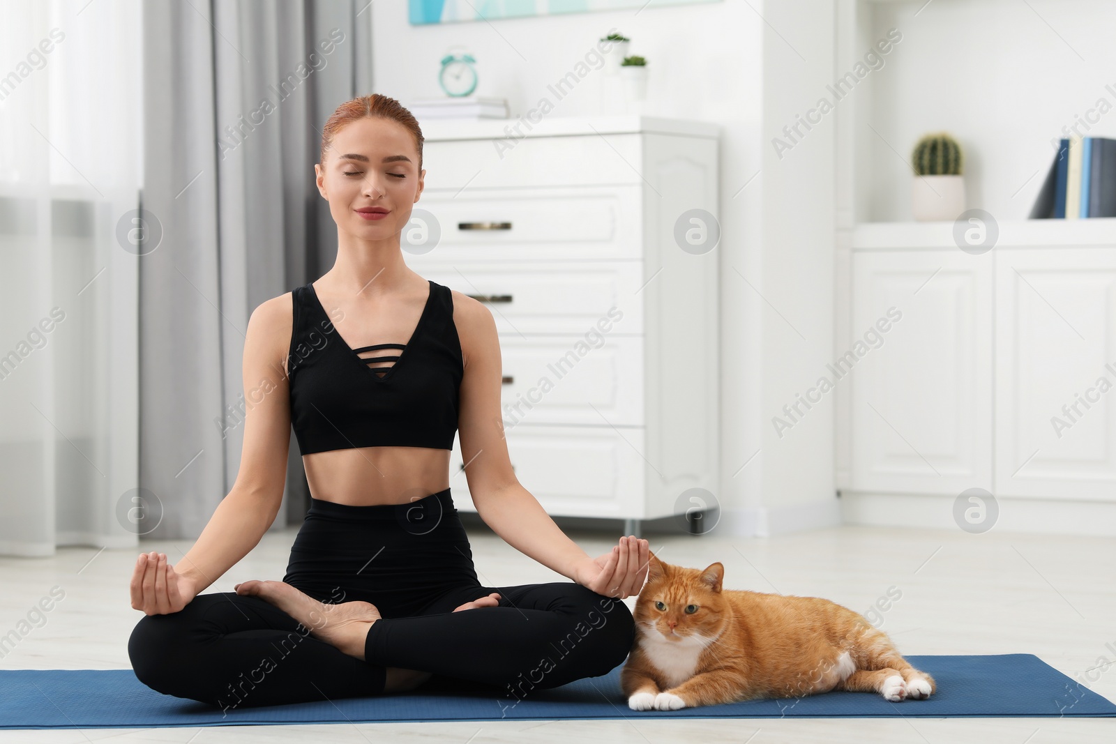 Photo of Beautiful woman with cute red cat practicing yoga on mat at home