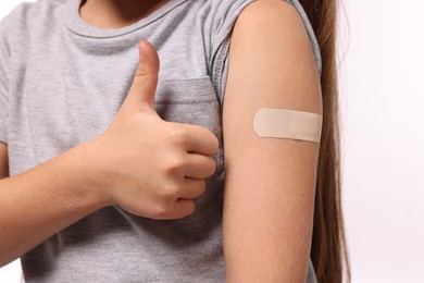 Photo of Girl with sticking plaster on arm after vaccination showing thumbs up against white background, closeup