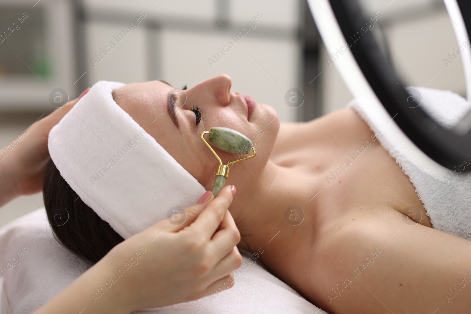 Photo of Cosmetologist making face massage with roller to client in clinic, closeup