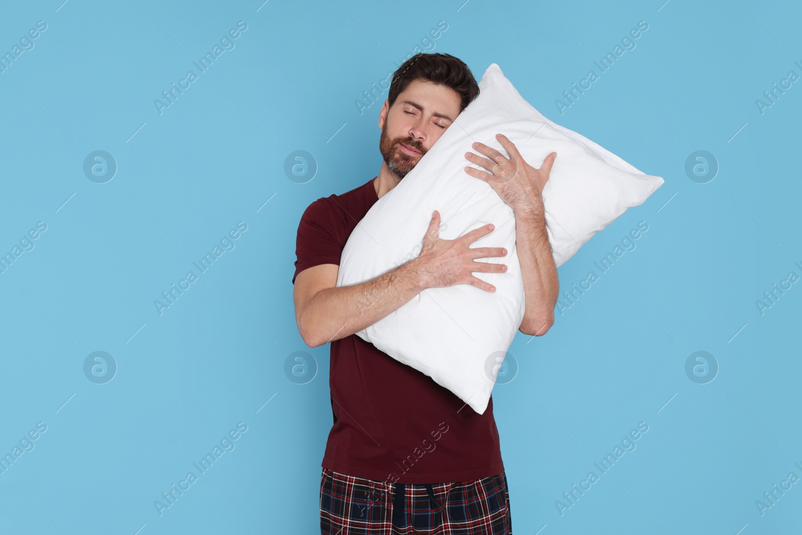 Photo of Sleepy handsome man hugging soft pillow on light blue background