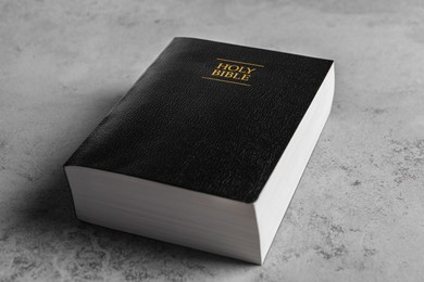 Photo of Bible with black cover on light gray table, closeup. Christian religious book