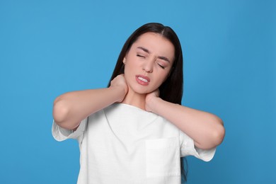 Photo of Young woman suffering from pain in neck on light blue background. Arthritis symptoms