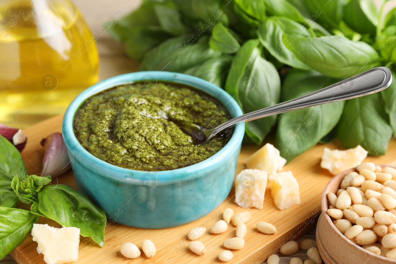 Photo of Tasty pesto sauce in bowl, basil, pine nuts, cheese and garlic on table, closeup