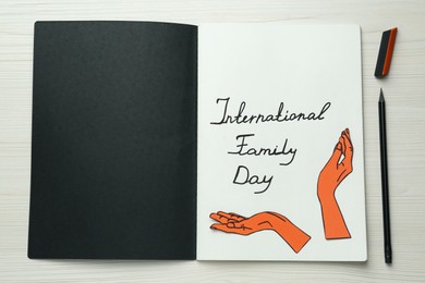 Photo of Happy Family Day. Notebook with written phrase, paper hands cutout and stationery on white wooden table, flat lay