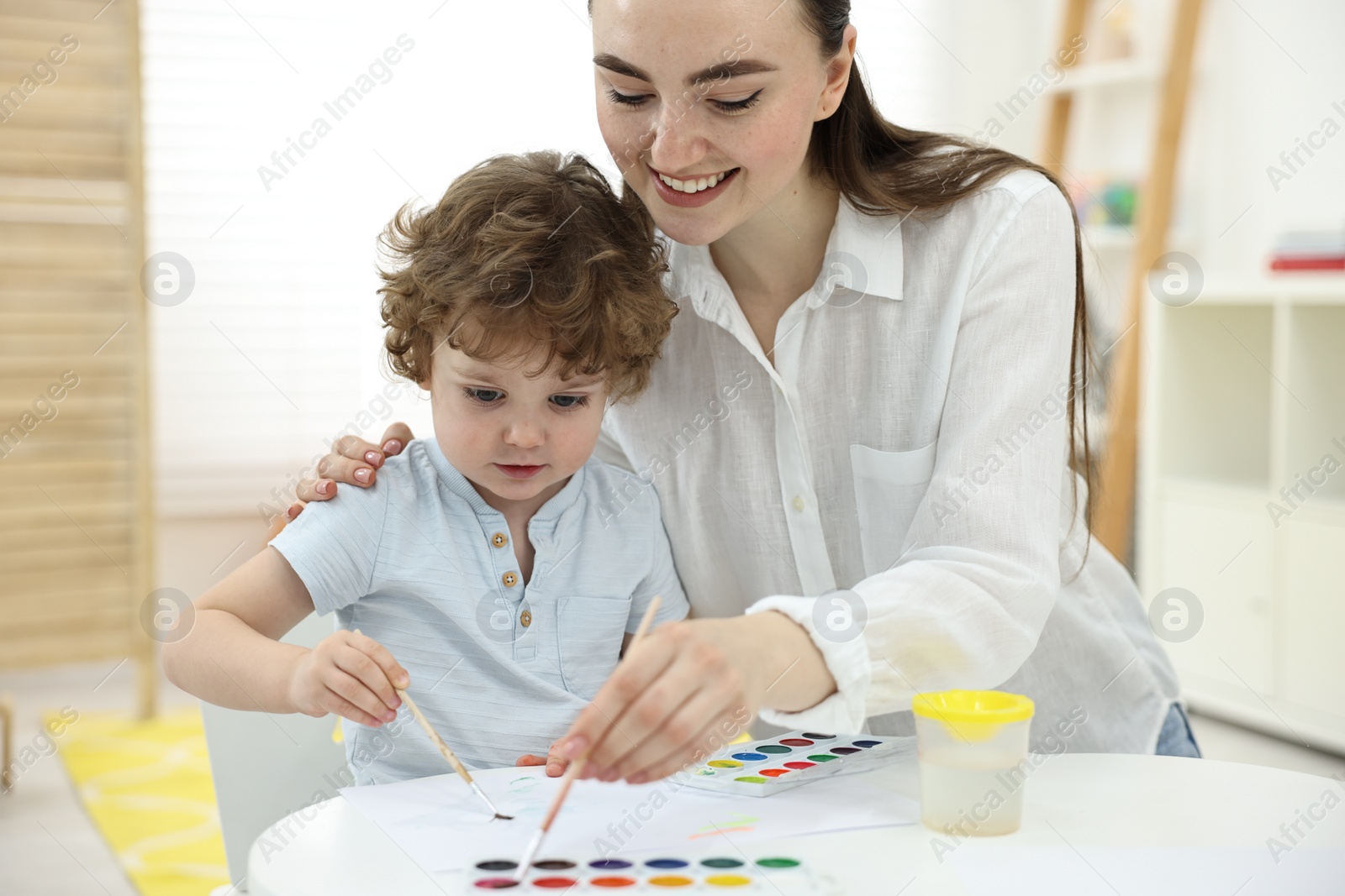 Photo of Mother and her little son painting with watercolor at home, closeup