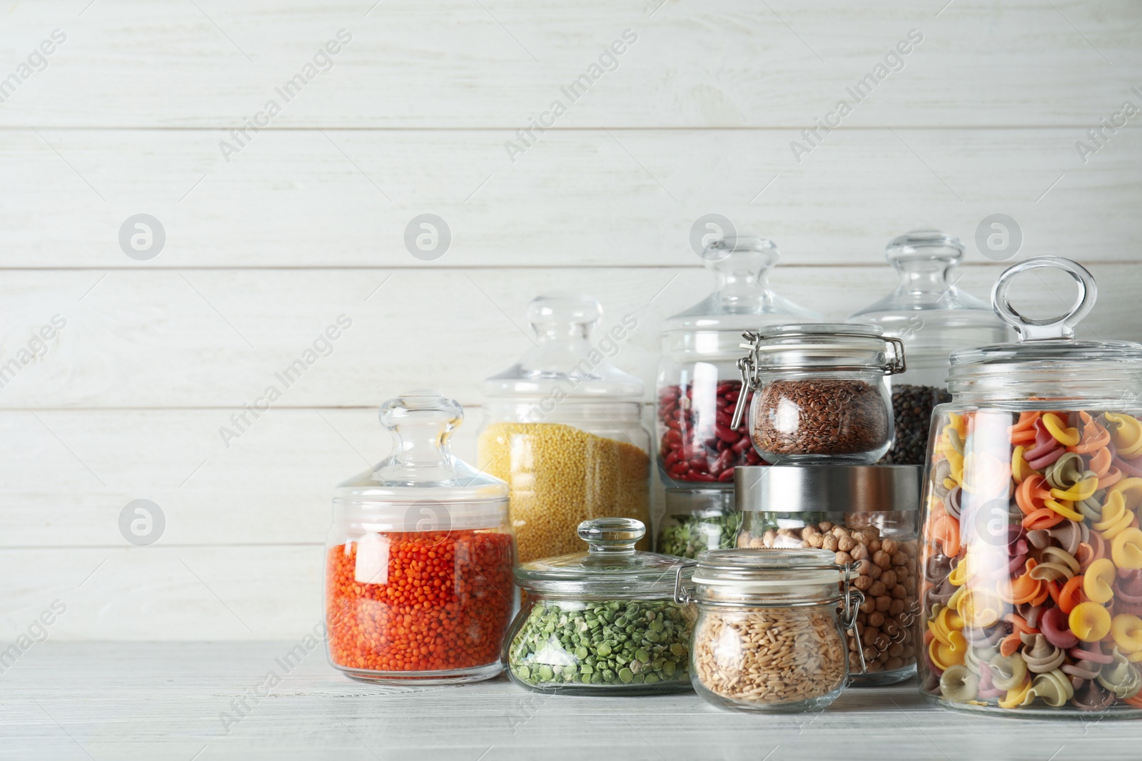 Photo of Glass jars with different types of groats and pasta on white wooden table