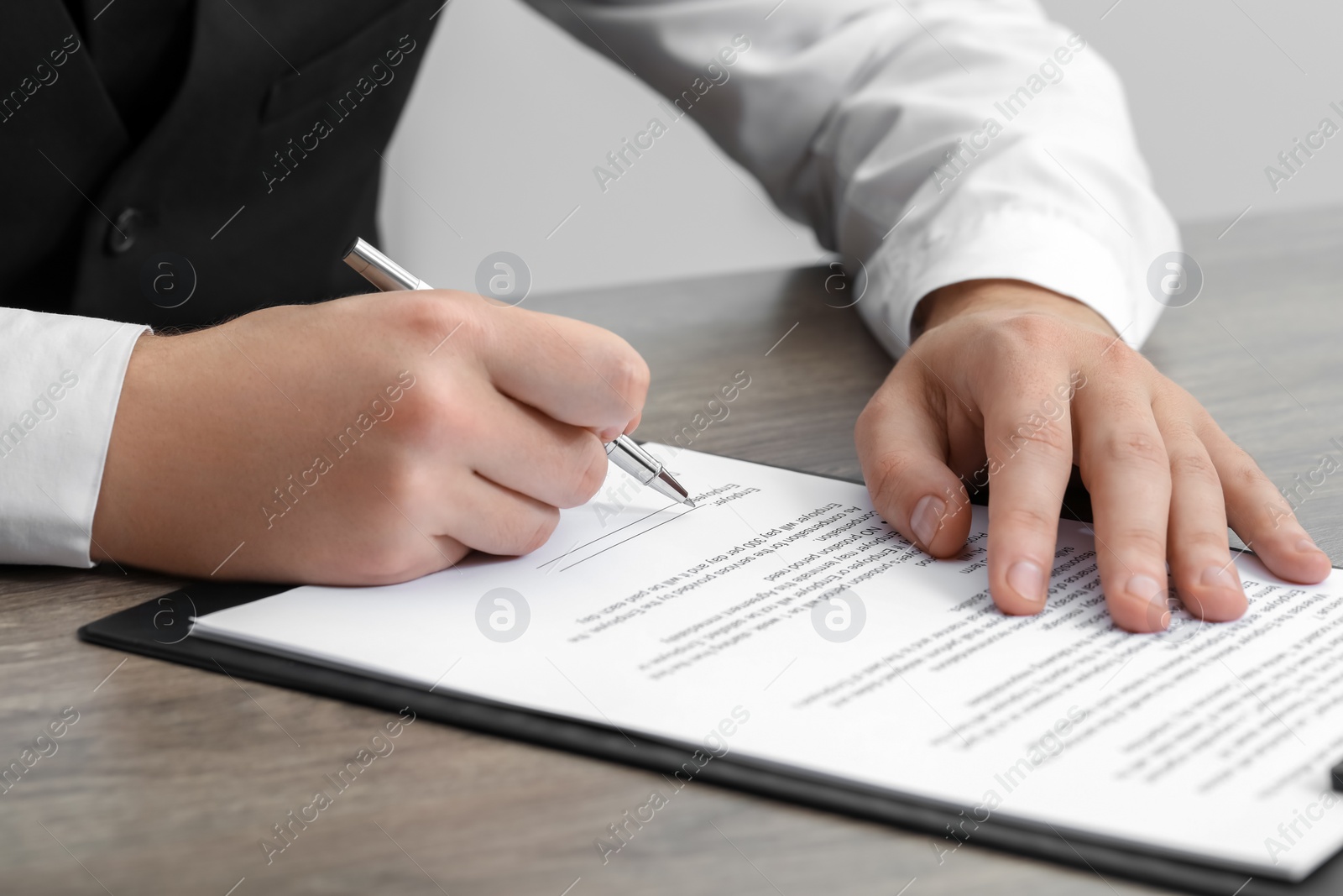 Photo of Man signing document at wooden table, closeup