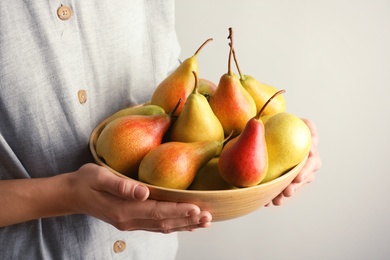 Photo of Woman holding bowl with ripe pears on light background, closeup