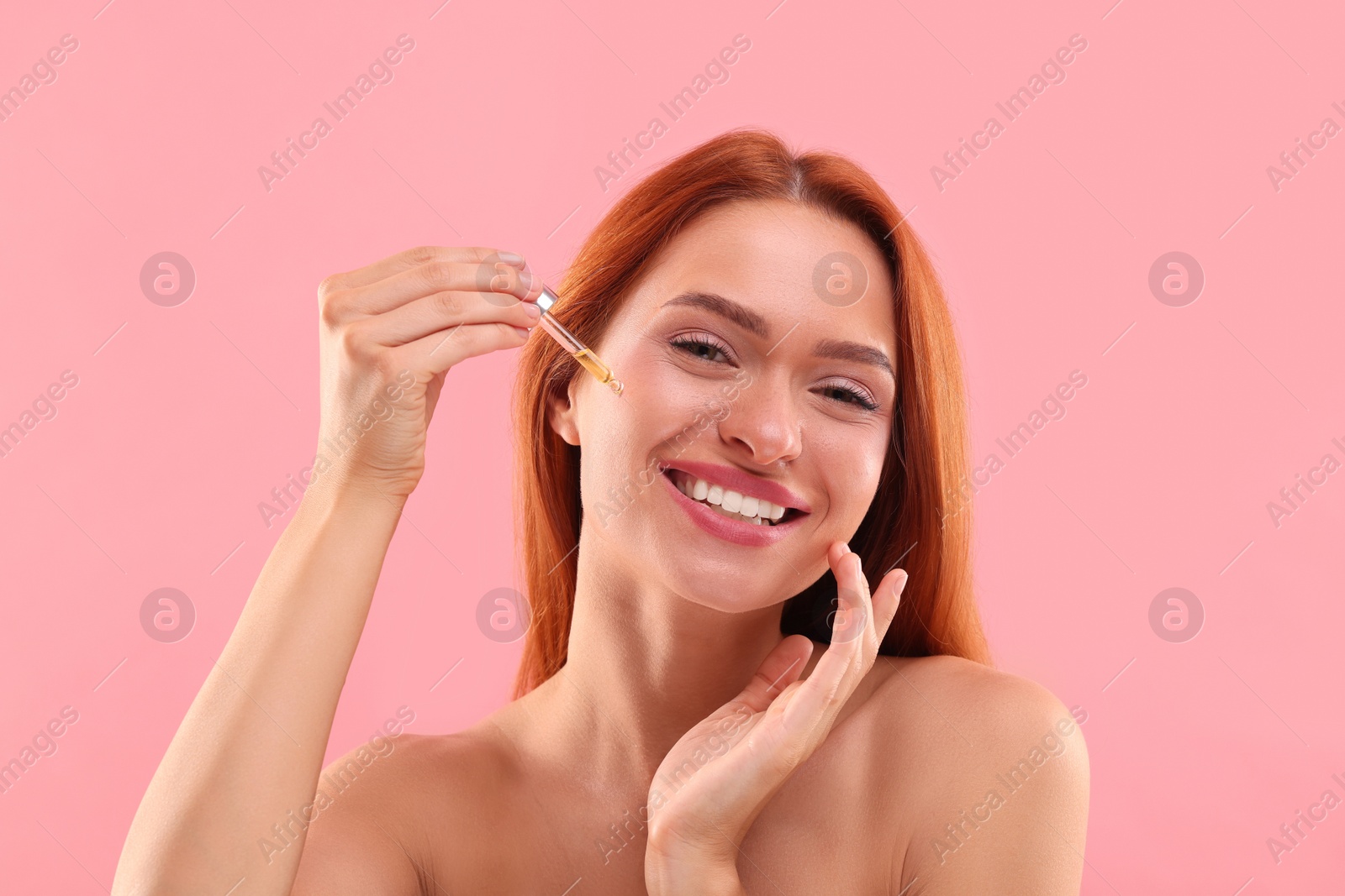 Photo of Beautiful young woman applying cosmetic serum onto her face on pink background