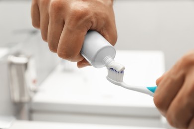 Man applying toothpaste on brush in bathroom, closeup
