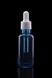 Photo of One blue bottle with tincture on mirror surface against black background