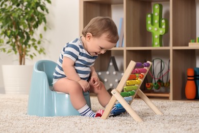 Photo of Little child with abacus sitting on plastic baby potty indoors
