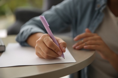 Photo of Woman writing letter at table indoors, closeup