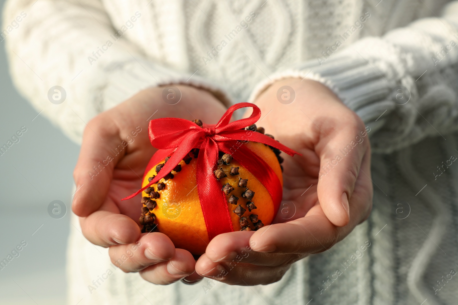 Photo of Woman holding pomander ball with red ribbon made of fresh tangerine and cloves on light background, closeup