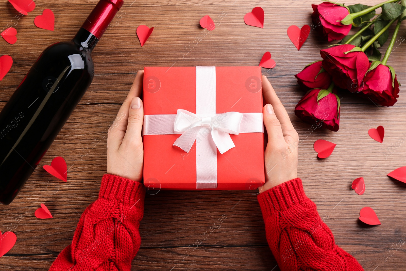 Photo of Woman holding beautiful gift box at wooden table, top view. Valentine's Day celebration