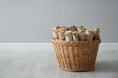 Wicker basket with firewood near grey wall indoors, space for text