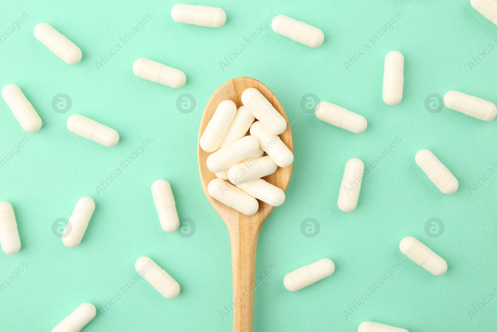 Photo of Wooden spoon with vitamin capsules on turquoise background, flat lay