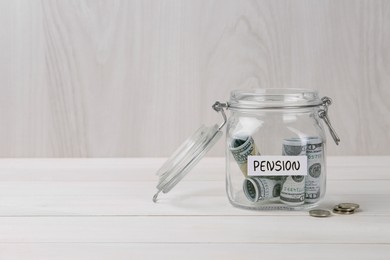 Photo of Glass jar with word Pension, coins and dollar banknotes on white wooden table. Space for text