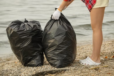 Photo of Woman with trash bags full of garbage on beach, closeup