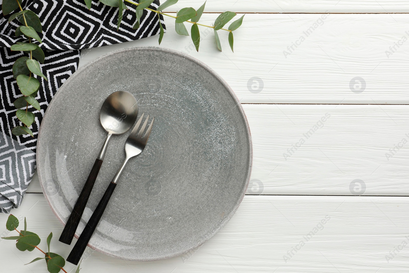 Photo of Stylish setting with cutlery, plate, napkin and eucalyptus branches on white wooden table, top view. Space for text