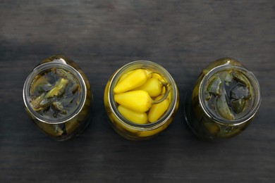 Photo of Glass jars of pickled green and yellow jalapeno peppers on wooden table, flat lay