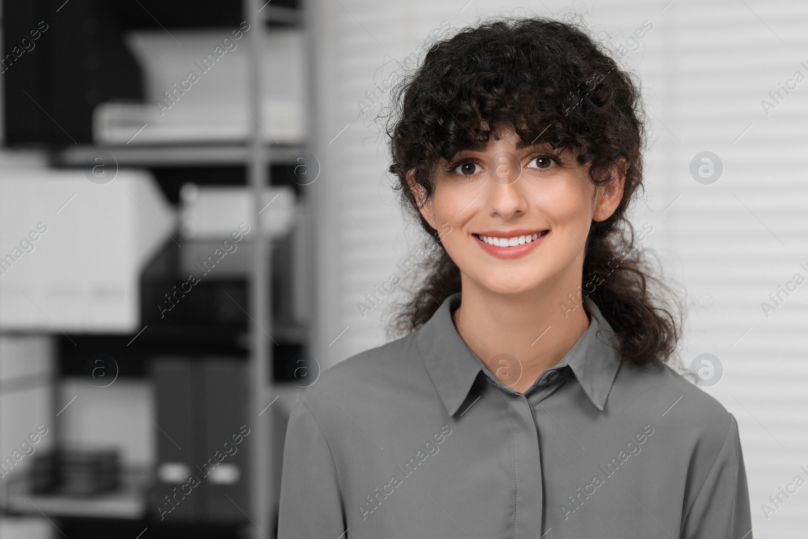Photo of Portrait of confident entrepreneur indoors. Beautiful lady with curly hair smiling and looking into camera. Space for text