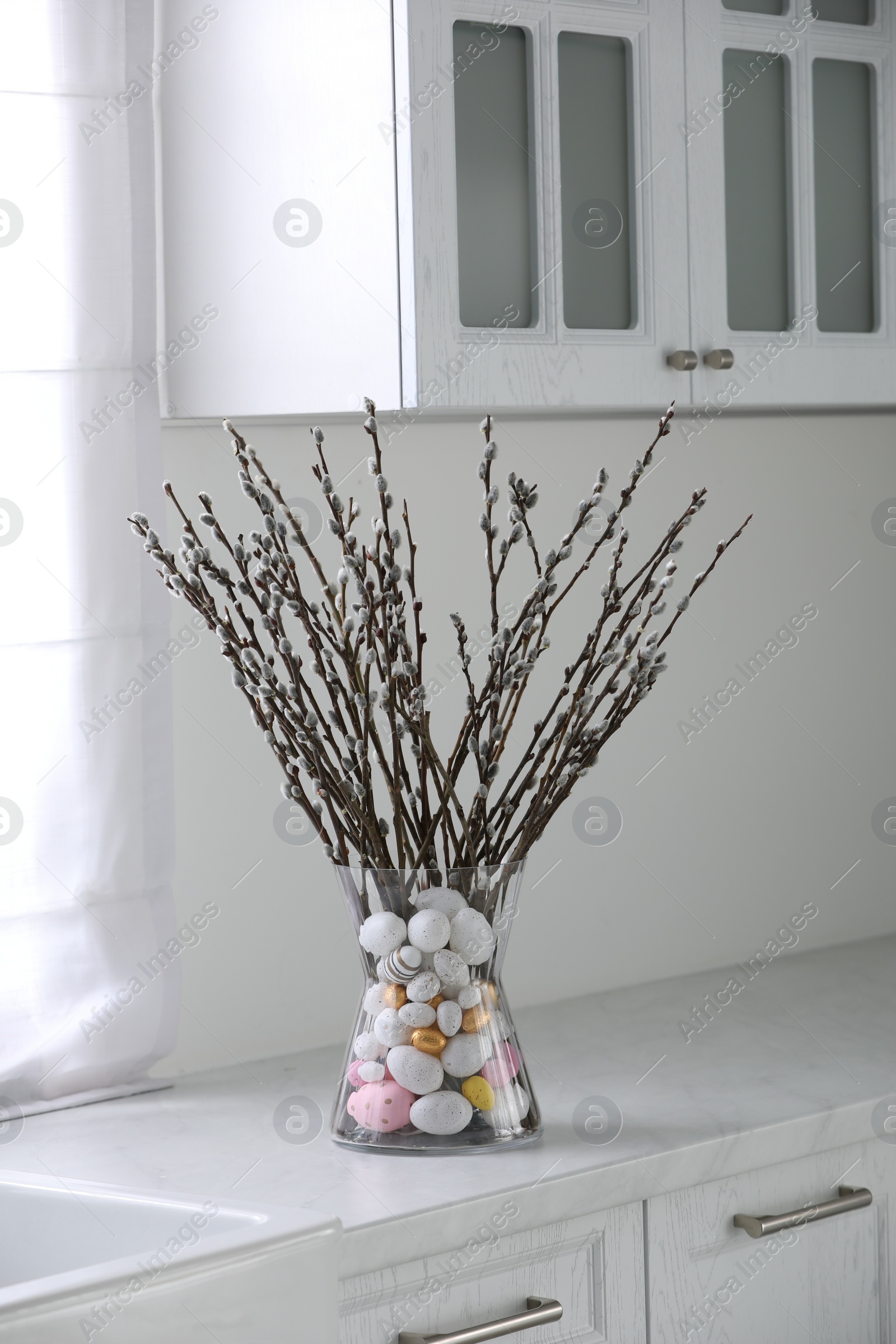 Photo of Vase with beautiful pussy willow branches and painted eggs on countertop in kitchen. Easter decor