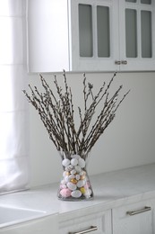 Vase with beautiful pussy willow branches and painted eggs on countertop in kitchen. Easter decor