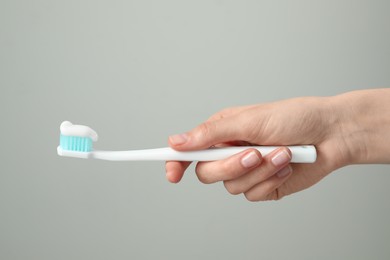 Woman holding toothbrush with paste on light grey background, closeup