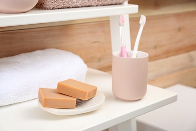 Photo of Soap bars, towel and toothbrushes on shelf in bathroom