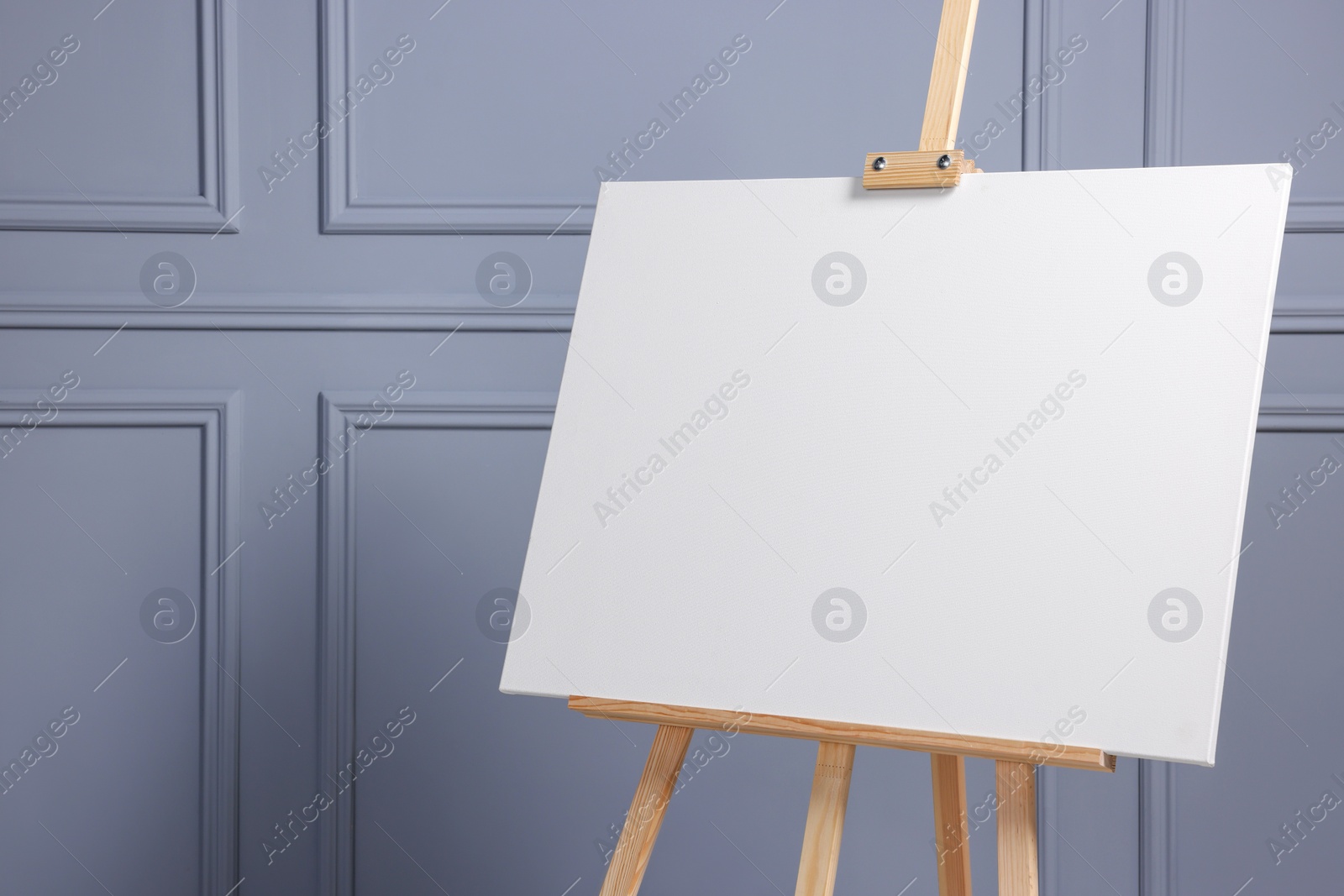 Photo of Wooden easel with blank canvas near grey wall indoors, closeup. Space for text