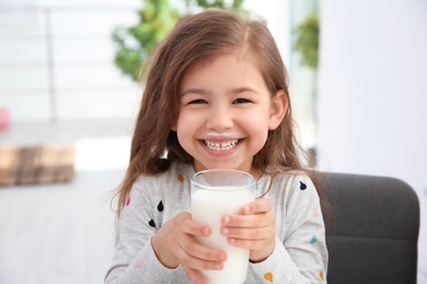 Cute little girl with glass of milk indoors