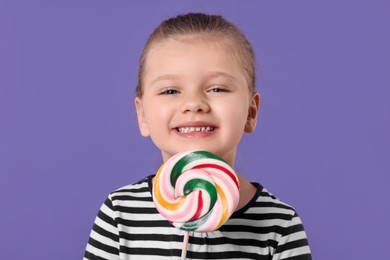 Photo of Happy little girl with colorful lollipop swirl on violet background