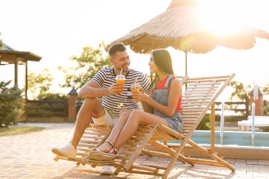 Image of Happy couple with cups of refreshing drink resting in deck chairs outdoors