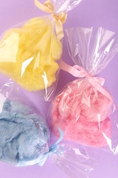 Photo of Packaged sweet cotton candies on violet background, flat lay