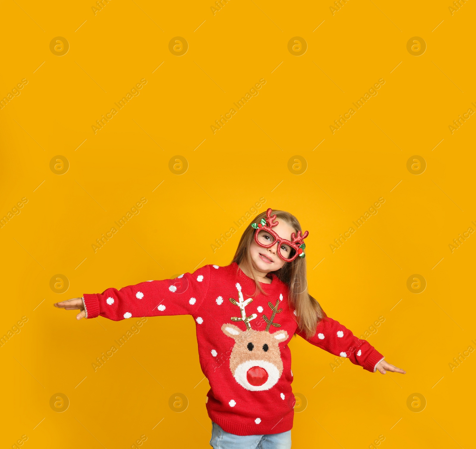 Photo of Cute little girl in Christmas sweater and party glasses on yellow background