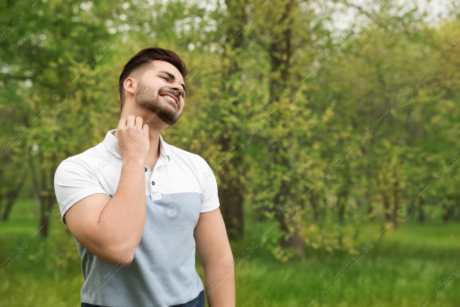 Photo of Young man scratching neck outdoors, space for text. Seasonal allergy