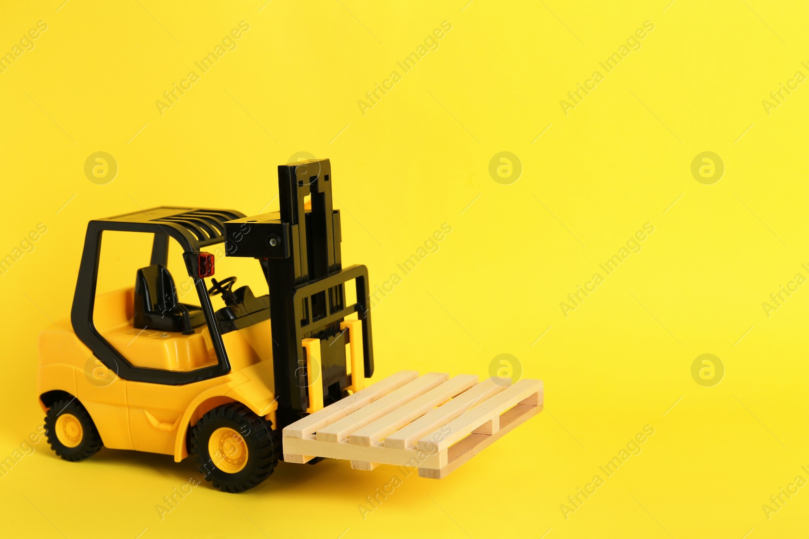 Photo of Toy forklift with wooden pallet on yellow background, space for text