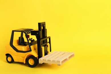 Photo of Toy forklift with wooden pallet on yellow background, space for text