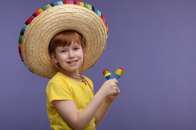 Photo of Cute boy in Mexican sombrero hat with maracas on violet background, space for text
