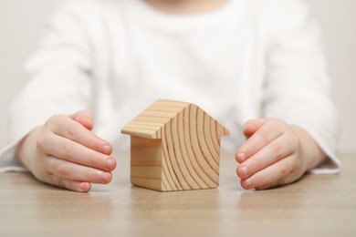 Photo of Home security concept. Little child with house model at wooden table, closeup