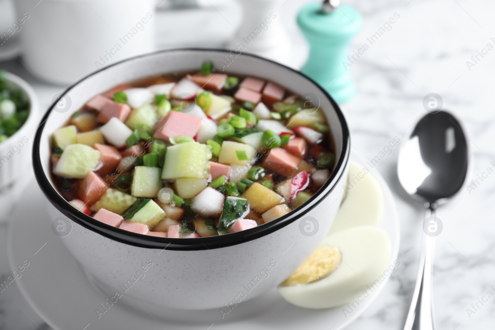 Photo of Delicious cold okroshka with kvass served on white marble table, closeup. Traditional Russian summer soup